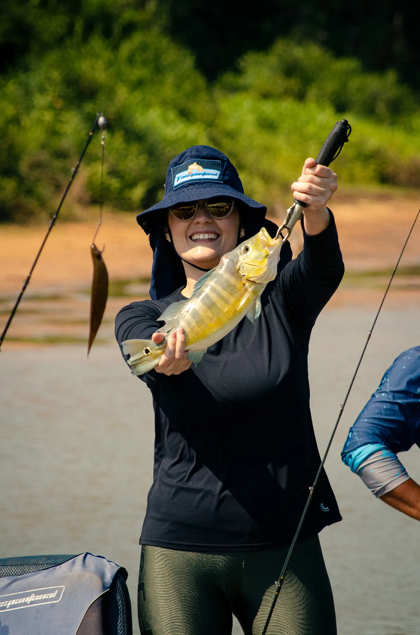 Pescadora sorrindo ao erguer um tucunaré fisgado no rio